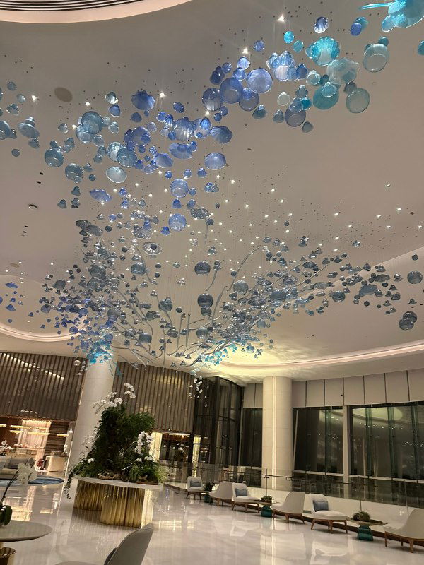 Просторный лобби отеля в Абу-Даби с декоративной потолочной инсталляцией из синих шаров и зелёными растениями, вечерняя атмосфера ресепшн.