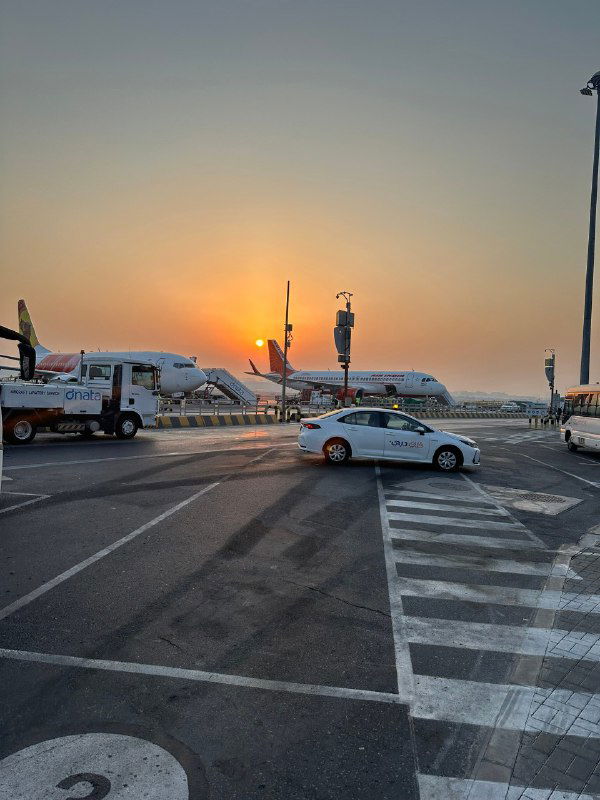 Закат в аэропорту: рулёжная дорожка, стоящие самолёты и такси на фоне оранжевого неба, момент перед вылетом домой.