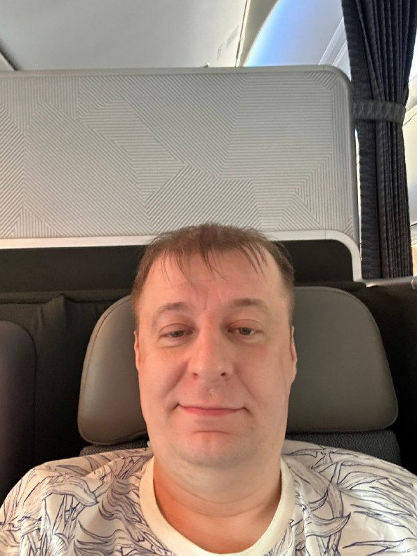 Селфи пассажира в салоне самолёта: мужчина в кресле с нейтральным выражением лица, кадр изнутри рейса после насыщенного дня.