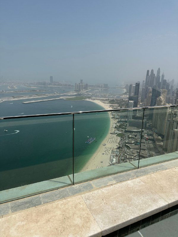 Панорамный вид с высотного этажа на изогнутую береговую линию, пляжи и современную городскую застройку на фоне морского горизонта.