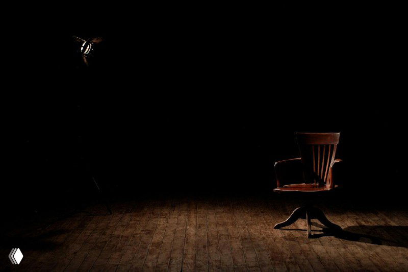 Пустой деревянный стул на тёмной сцене в луче света, композиция с акцентом на ожидание и фокус — символ подготовки к выступлению и демонстрации навыков.