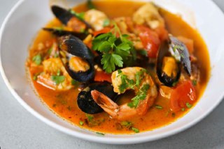 Порция рыбного супа по‑сицилийски в тарелке: мидии, креветки, кусочки рыбы и зелень в насыщенном томатном бульоне