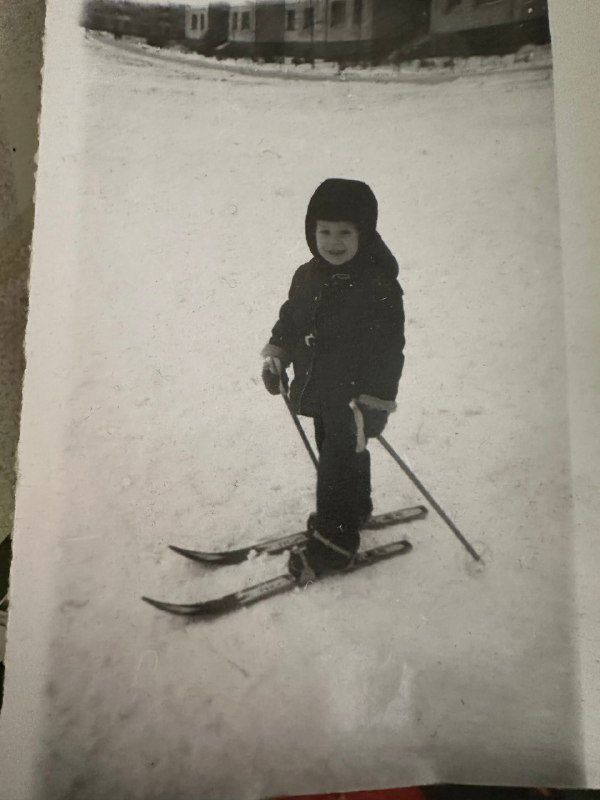Чёрно-белая фотография ребёнка на лыжах в снегу; архивный семейный кадр, детство во дворе, зимняя сцена, без точных временных меток.