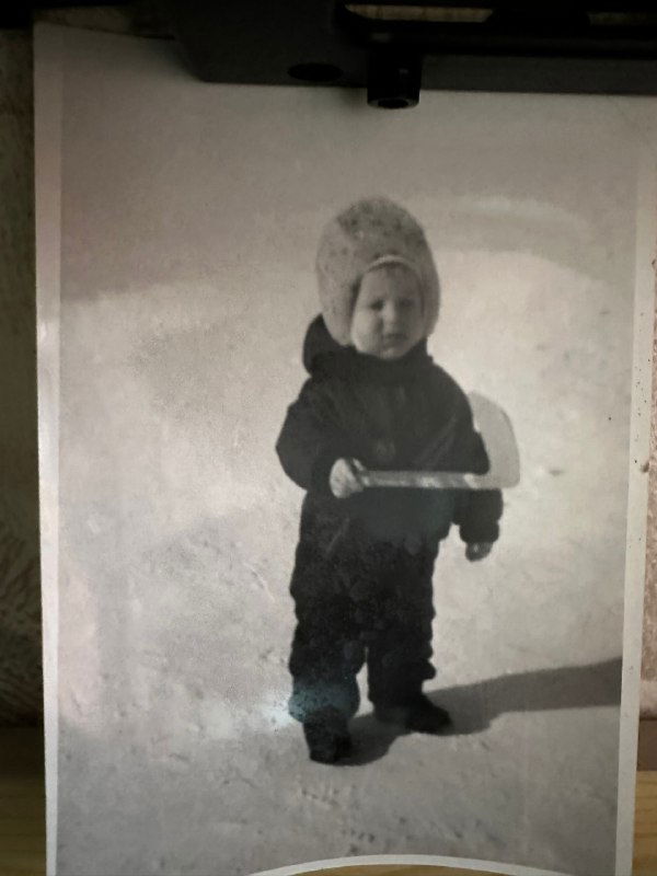 Чёрно-белая фотография маленького ребёнка в шапке, стоит в снегу с игрушкой; архивный снимок советского детства, домашняя атмосфера, без лицевых подписей.