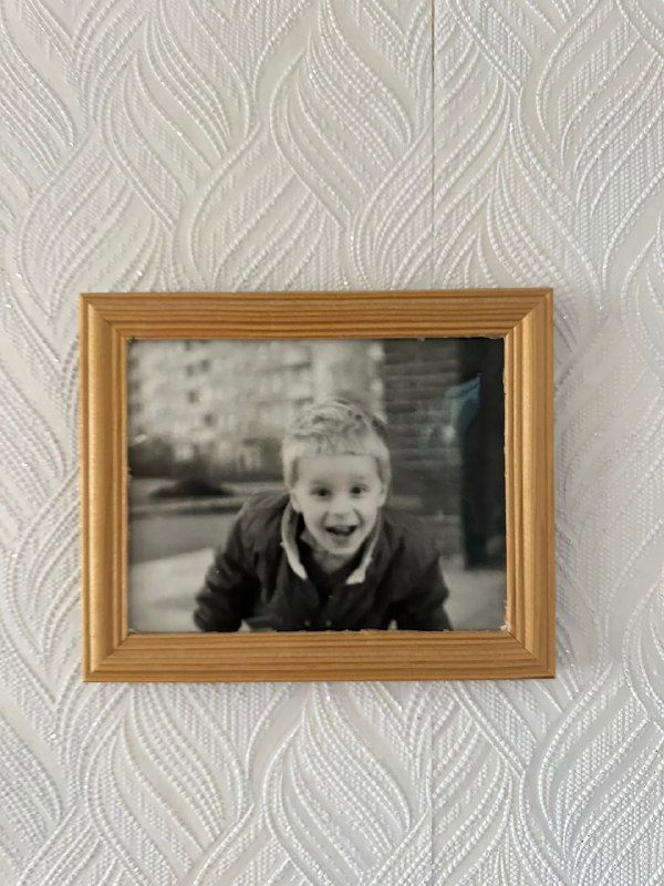Фотография в рамке на стене: детский портрет в чёрно-белом стиле; семейный снимок в интерьере, ностальгический элемент домашнего архива, без метаданных.