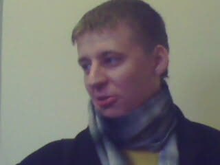 Кадр молодого мужчины в шарфе и тёмной одежде, сделан в помещении; личный архивный снимок повседневного характера, без указания личности.