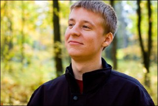 Портрет молодого мужчины, снятый в парке с боковым освещением; видна лёгкая улыбка и размытый природный фон, снимок в поясной/грудной план