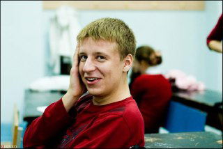 Мужчина в повседневной одежде в помещении, видна обстановка типа аудитории или рабочего пространства, кадр средний, непринуждённая поза