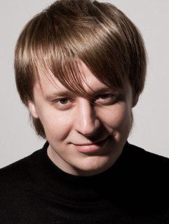 Студийный портрет молодого мужчины на нейтральном фоне с характерной причёской и тёмной водолазкой, крупный план лица и плеч