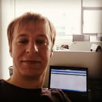 Селфи у рабочего стола с открытым монитором и офисным окном на заднем плане; кадр показывает рабочую обстановку и экран с приложением.