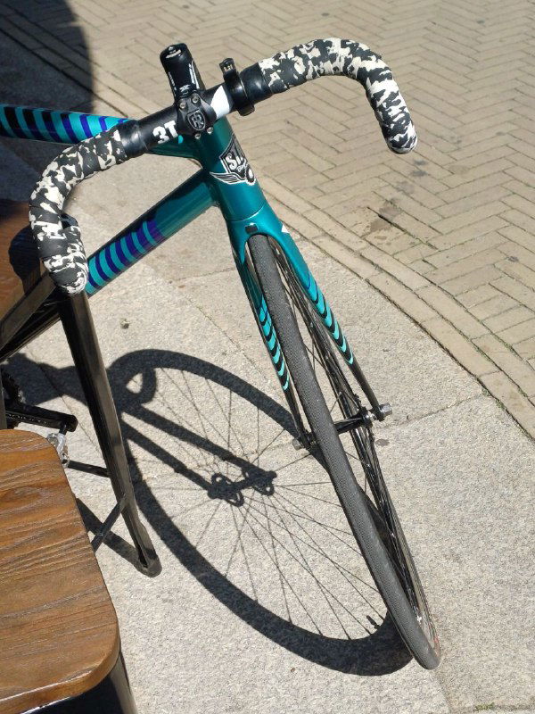 Крупный план рулевой колоды и переднего колеса трека Undefeated — видна карбоновая вилка, оформление обмотки и дорожное покрытие рядом.