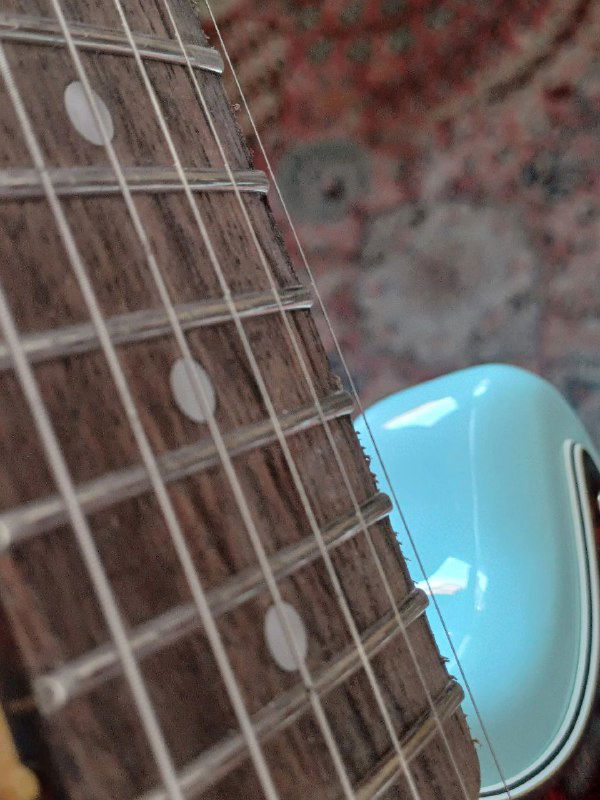 Крупный план грифа и нижней части корпуса Squier Mustang: видны неровные лады, пятна на струнах и фактура накладки.