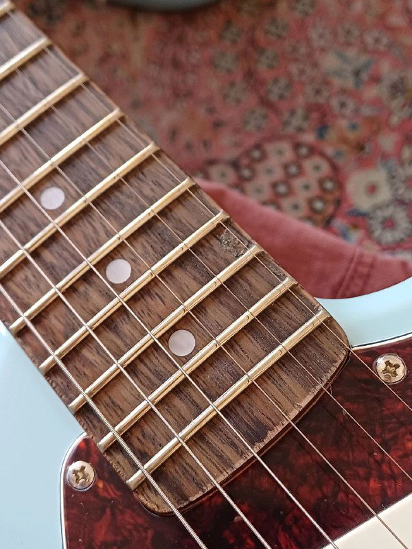 Крупный кадр грифа Squier Mustang: изношенные и кривые лады, потертости вокруг ладов и следы ремонта на накладке.