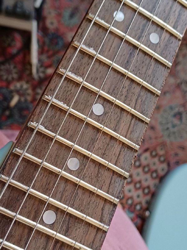 Детальный снимок накладки грифа Squier Mustang: пятна, царапины и неровности ладов, указывающие на дефекты качества.