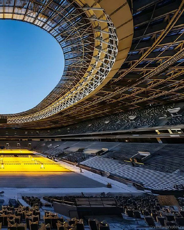 Ещё один крупный план арены/стадиона в тёплых тонах, используемый как визуальный акцент в шаблоне поста о недвижимости рядом со спортивной инфраструктурой.