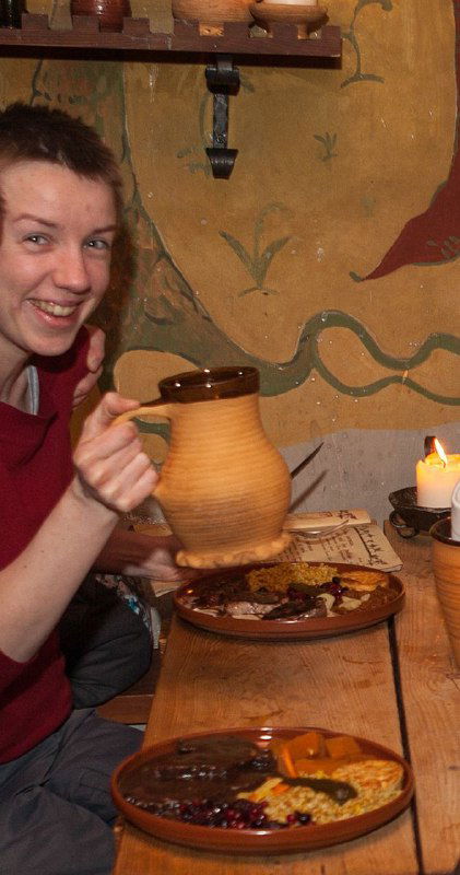 Человек улыбается и держит кувшин рядом с тарелками с едой на деревянном столе в тёплой домашней обстановке, сцена общения.