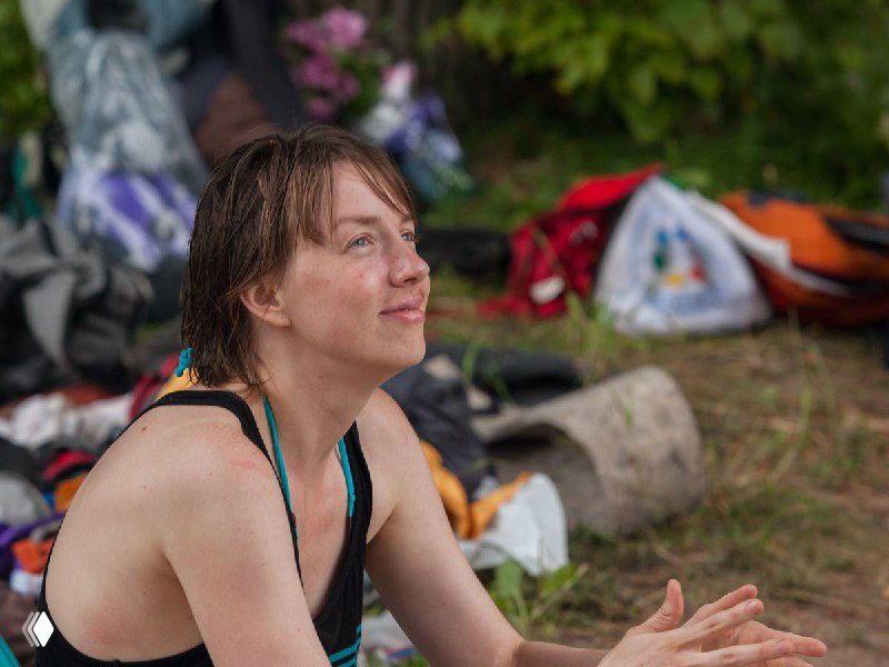 Человек на природе улыбается, сидит на земле рядом с рюкзаками и вещами, момент отдыха, восстановления и простого облегчения после испытаний.