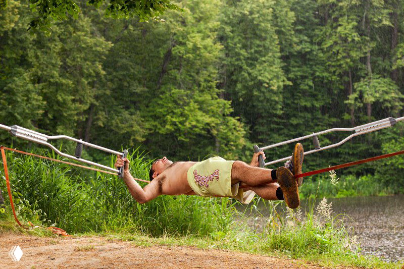 Человек лежит в гамаке у воды на фоне зелёного леса, расслабленное тело, летний день, кадр про восстановление и релаксацию на свежем воздухе.