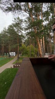 Балкон с деревянными перилами, в руке чашка; на заднем плане сосновый лес, дорожка и лавочки — спокойный контекст для размышлений и работы.