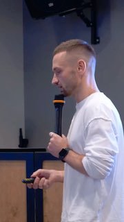 Мужчина в белой футболке держит микрофон и пульт во время выступления в помещении — боковой профиль, деловая атмосфера