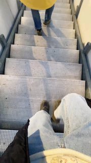 Фото металлической лестницы сверху: в кадре ступени и ноги людей в повседневной одежде, атмосферный снимок коридора места проведения.