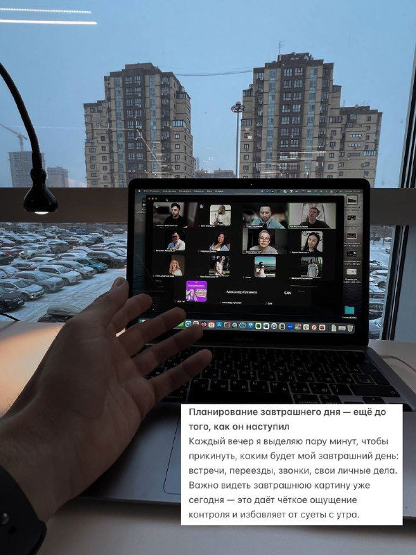 Ноутбук с включённой видеоконференцией на рабочем столе у окна с видом на город; кадр подчёркивает планирование загруженного дня и рабочие сессии утром.