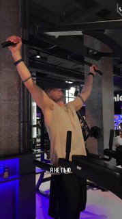 Вертикальное фото мужчины в спортивной рубашке в тренажёрном зале с поднятыми руками; на кадре видна надпись «Я не пью», что создаёт контекст личного выбора.