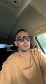 Человек в солнцезащитных очках делает селфи в салоне автомобиля; кадр показывает потолок, окно и часть бокового стекла на превью анонса.