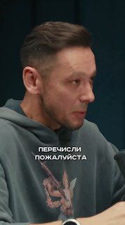 Кадр подкаста: боковой портрет мужчины в серой худи за микрофоном, на худи видна надпись «ПЕРЕЧИСЛИ ПОЖАЛУЙСТА».