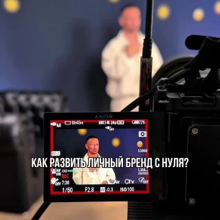 Кадр через экран видеокамеры: спикер на сцене в фокусе, на экране видна надпись «Как развить личный бренд с нуля?», студийная постановочная съемка.