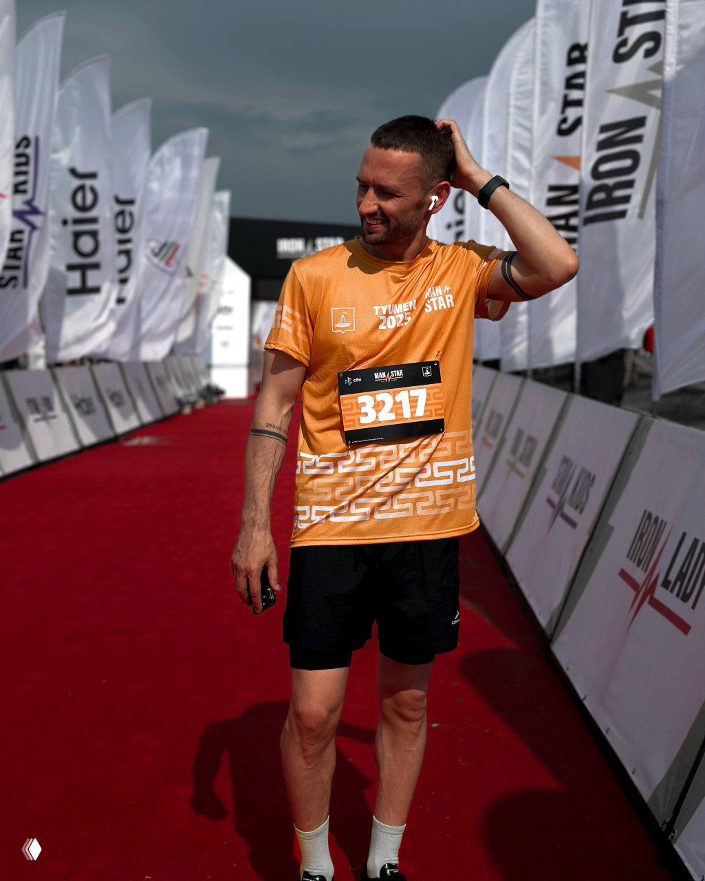 Мужчина в спортивной форме пересёк финишную зону забега, на груди номер; кадр демонстрирует участие в спортивных соревнованиях и активный образ жизни.