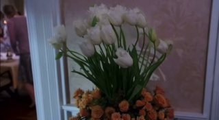 Большой букет белых тюльпанов и оранжевых цветов на столе на фоне нежно-розовых обоев — интерьерный фрагмент, подчёркивающий аккуратность и эстетику дома.