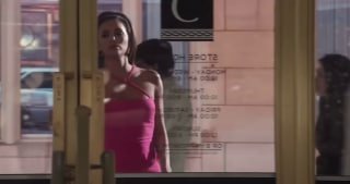 Женщина в розовом платье отражается в витрине и двери — городской кадр из сериала, символизирующий дистанцию между образом и внутренним миром Габи.