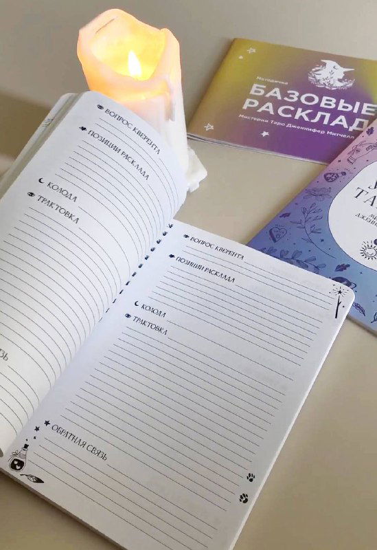 Открытый блокнот с шаблонами для записи раскладов Таро: видны поля для интерпретаций, пометок и дат; рядом свеча и учебный буклет.