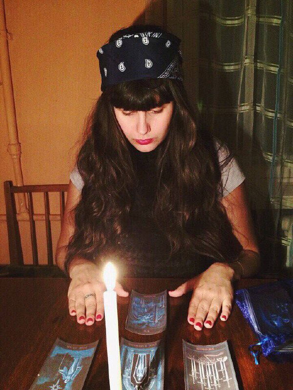 Женщина проводит расклад Таро при зажжённой свече, карты разложены на столе в тёмной комнате — практическая демонстрация метода.