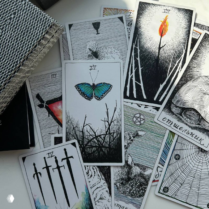 Крупный план нескольких карт колоды: бабочка на одной карте, факельный Жезл и черно-белая графика с цветными акцентами на деталях.