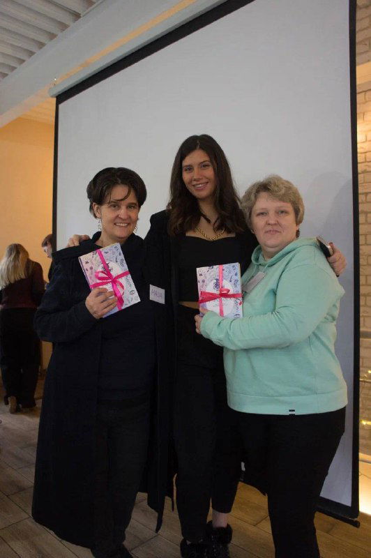 Фото преподавателя с двумя участницами, все улыбаются и держат подарки — момент завершения практической сессии и награждения.