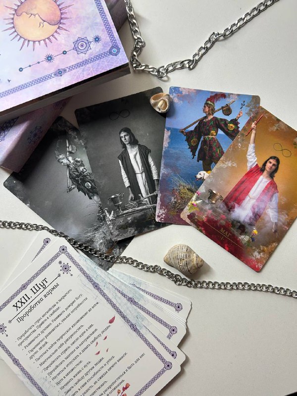 Разложенные карты колоды Life Spirit: на фото цветные и чёрно‑белые версии арканов рядом с коробкой, маленькими ракушками и металлической цепочкой.