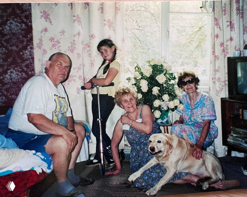 Семейная фотография в комнате: дедушка, бабушка, женщина и собака рядом с елкой и бытовой техникой — уют и близкие люди.