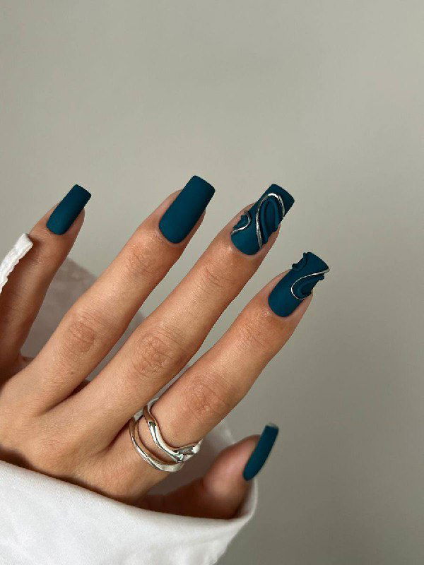 Рука с матовым тёмно-синим маникюром и абстрактными серебристыми акцентами, аккуратные квадратные ногти, минималистичный фон.