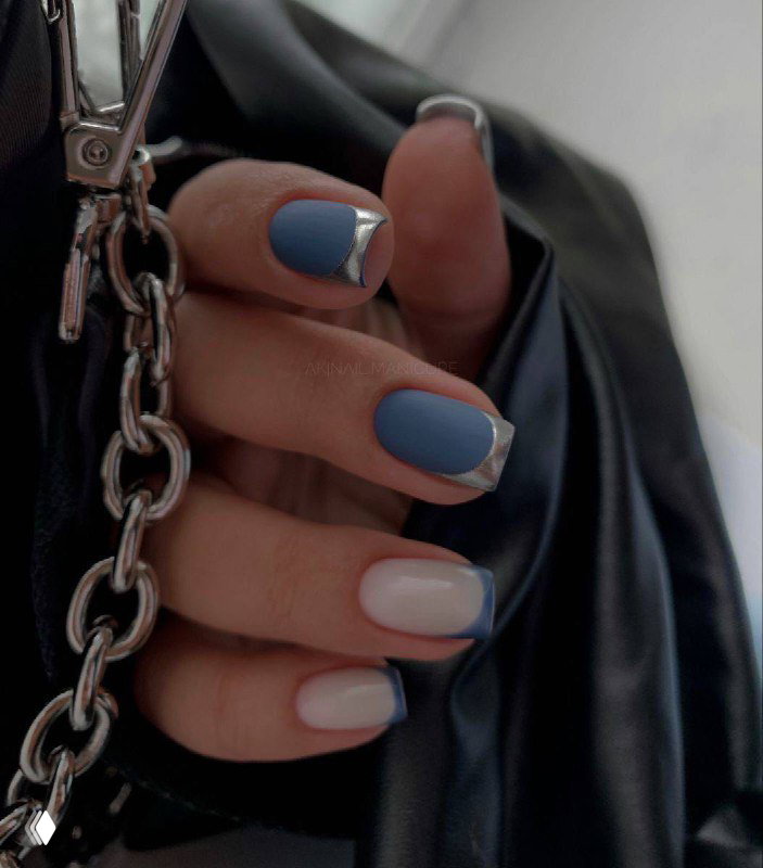 Крупный план руки с овальными ногтями в голубо-белых тонах и металлической цепочкой на фоне чёрной одежды, контрастный стиль.