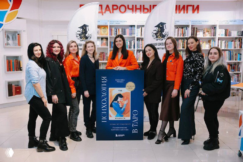 Группа участниц вместе с автором у стенда с рекламой книги в книжном магазине — совместная фотография с презентации мероприятия.