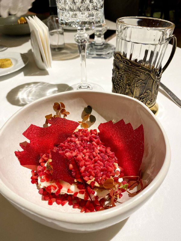 Крупный план десерта: яркая красная кондитерская композиция на белой тарелке и элегантная сервировка стола с бокалами и подстаканником.