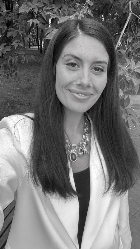 Черно‑белая версия портретного снимка автора на фоне деревьев: спокойное выражение лица, белый пиджак и украшение; стилизованная фотовариация для поста.