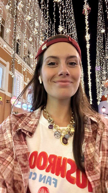 Фотография автора в ночном городе: женщина улыбается на фоне ярких огней, кепка надвинута назад, атмосфера тёплой вечерней иллюминации.