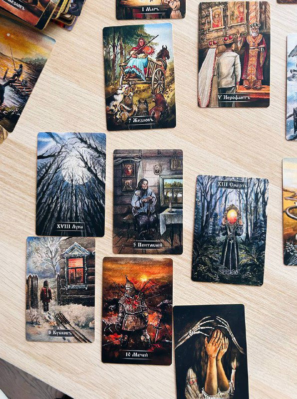 Групповой снимок карт Таро на столе: сцены с огнём, деревьями и человеческими фигурами, тёмные и светлые композиции соседствуют.