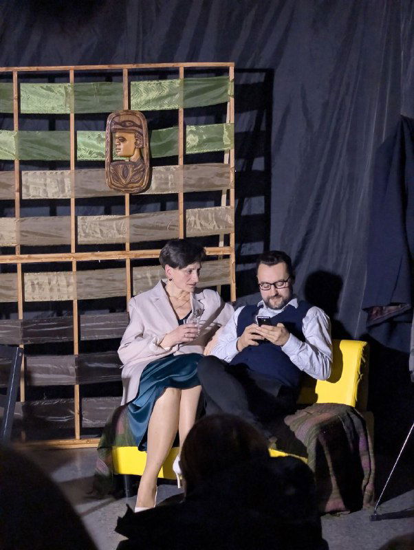 Два актёра на кресле и диване на фоне деревянной декорации: момент сценического диалога на новой малой сцене в Твери.