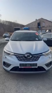 Передняя часть серебристого кроссовера Samsung XM3 на стоянке; кадр иллюстрирует состояние автомобиля перед отправкой и окружающую площадку.