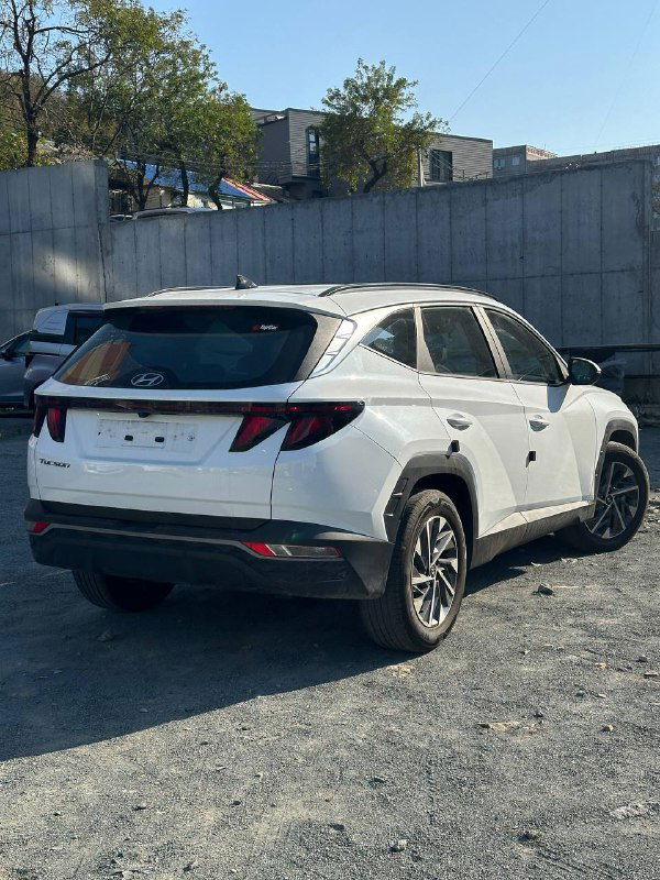 Задний вид белого Hyundai Tucson 2020 без регистрационного номера на стоянке, видно оформление фонарей, багажник и общую геометрию кузова перед отправкой клиенту.