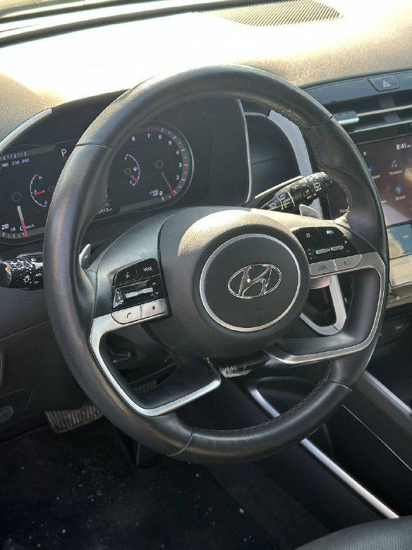 Крупный план рулевого колеса и панели приборов Hyundai Tucson: эмблема Hyundai, спидометр и элементы управления в салоне, состояние внутренней отделки видно для оценки клиента.